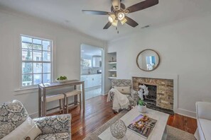 Ein Wohnzimmer mit Kamin, Deckenventilator, Essbereich mit Tisch und Stühlen sowie Blick in die Küche.