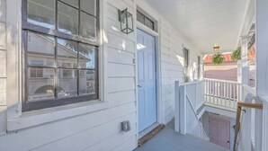 A white building with a blue door, a covered porch, and a staircase leading to an upper level. - 1880's Charleston Single. One Bedroom with parking (Charleston)