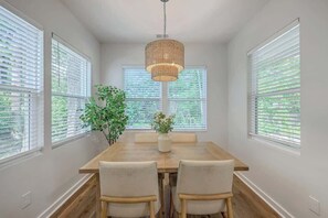 A dining area with a wooden table, two chairs, a hanging light fixture, and a potted plant. - Pilgrim Luxury #3. Newly Built! (Hanahan)
