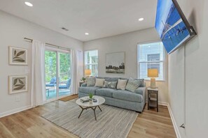 A living room with a grey sofa, a coffee table, a flat-screen TV, and a large window with blinds. - Pilgrim Luxury #3. Newly Built! (Hanahan)
