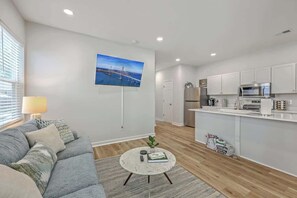 A modern living room with a sofa, a coffee table, and a TV mounted on the wall. - Pilgrim Luxury #3. Newly Built! (Hanahan)
