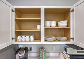 A kitchen with white cabinets, a coffee maker, and stacked plates. - Pilgrim Luxury #3. Newly Built! (Hanahan)