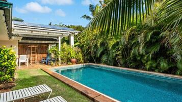 Une piscine entourée d’une terrasse en bois, de chaises longues et d’une végétation tropicale luxuriante.