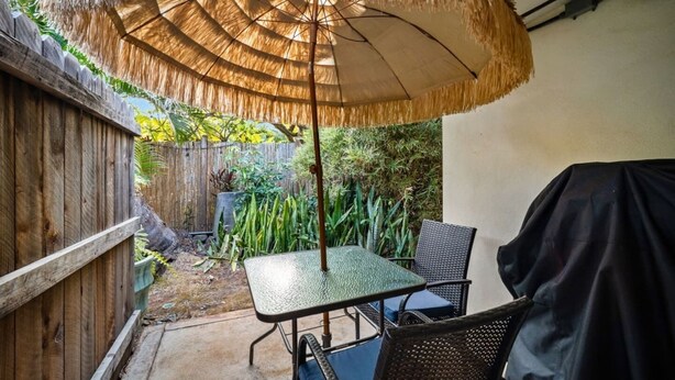 A patio with a table and chairs, a thatched umbrella, and a wooden fence.
