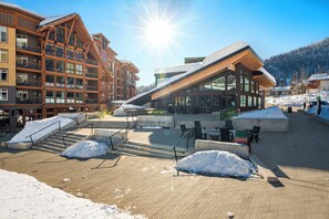 En modern byggnad med stora fönster, ett sluttande tak och ett område med snö som är belagt med tegelstenar.