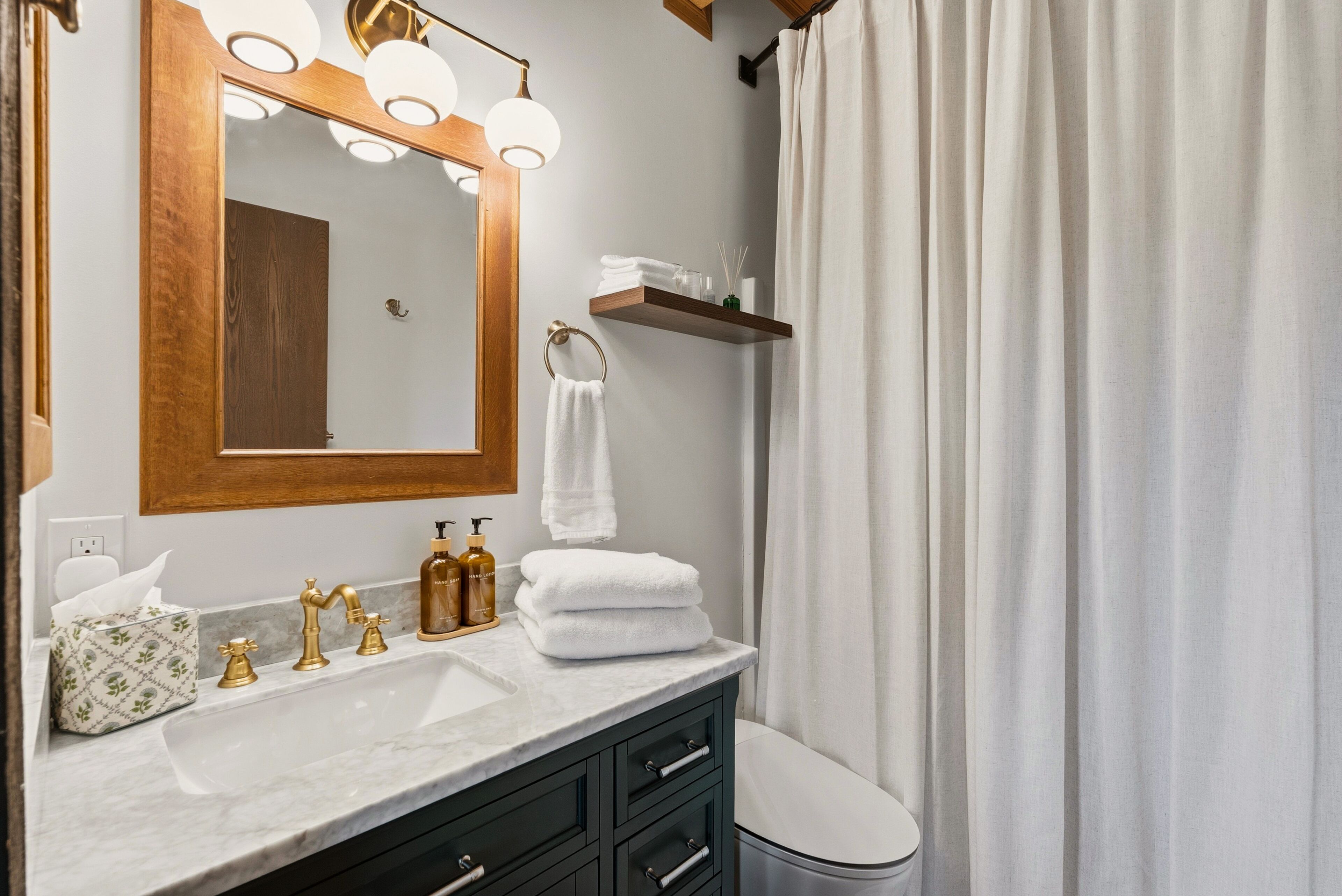 A bathroom with a marble sink, gold faucets, a wooden mirror, and a white toilet.