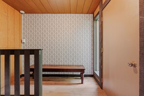 Een kamer met behang met een patroon, een houten bankje en een deur.