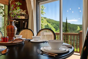 A dining table set with white plates, bowls, and cutlery, with a view of a mountainous landscape through large windows. - Schweitzer Mtn. Retreat -Chalet 75-w/Hot Tub Room + Lift Pass (Sandpoint)