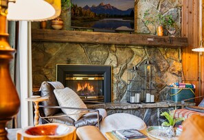 A cozy living room with a fireplace, comfortable seating, and a stone wall. - Schweitzer Mtn. Retreat -Chalet 75-w/Hot Tub Room + Lift Pass (Sandpoint)
