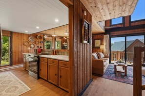 A modern kitchen with wooden cabinets, a built-in oven, and a dining area with a sofa and table. - Schweitzer Mtn. Retreat -Chalet 75-w/Hot Tub Room + Lift Pass (Sandpoint)