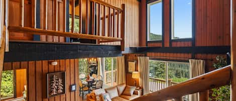 A multi-level wooden interior with a staircase, a dining area, and large windows offering views of the outdoors.