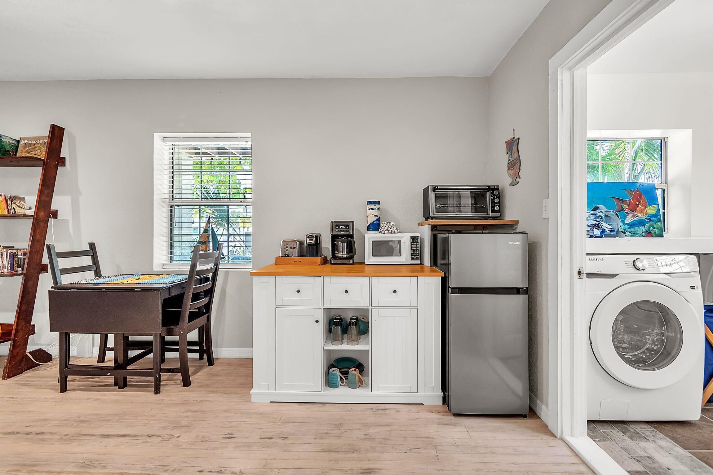 Une cuisine compacte comprenant une table à manger, des chaises, un four à micro-ondes, une machine à café, un réfrigérateur et un lave-linge.