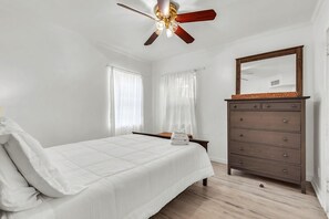 A bedroom with a bed, a dresser, a ceiling fan, and a large mirror. - Caddy's Cottage #1 (Treasure Island)
