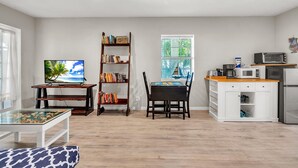 A living room with a TV, bookshelf, dining table, and kitchen area. - Caddy's Cottage #1 (Treasure Island)