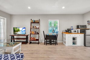 A living room with a TV, bookshelf, dining table, and kitchen area. - Caddy's Cottage #1 (Treasure Island)