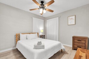 A hotel room with a bed, a wooden nightstand, a ceiling fan, and a framed picture on the wall. - Caddy's Cottage #1 (Treasure Island)