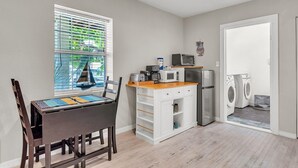A compact kitchen with a microwave, toaster, and refrigerator, a dining area with a table and chairs, and a laundry area with washing machines. - Caddy's Cottage #1 (Treasure Island)