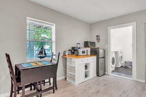 A compact kitchen with a microwave, toaster, and refrigerator, a dining area with a table and chairs, and a laundry area with washing machines. - Caddy's Cottage #1 (Treasure Island)