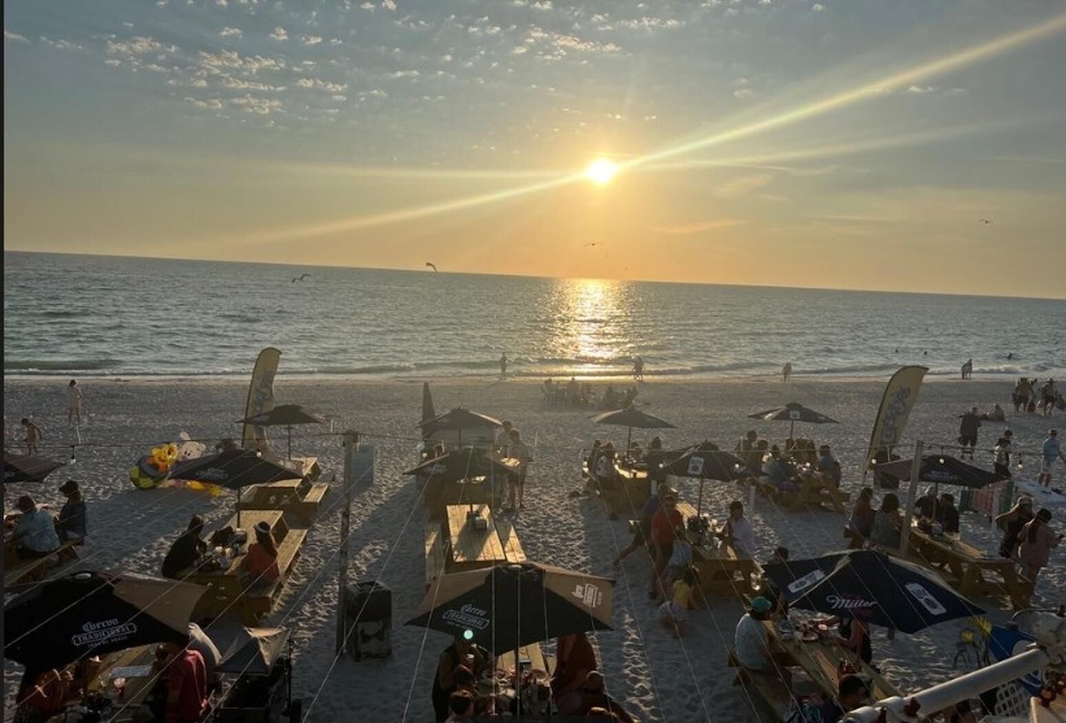 Een strand met parasols, ligbedden en mensen.