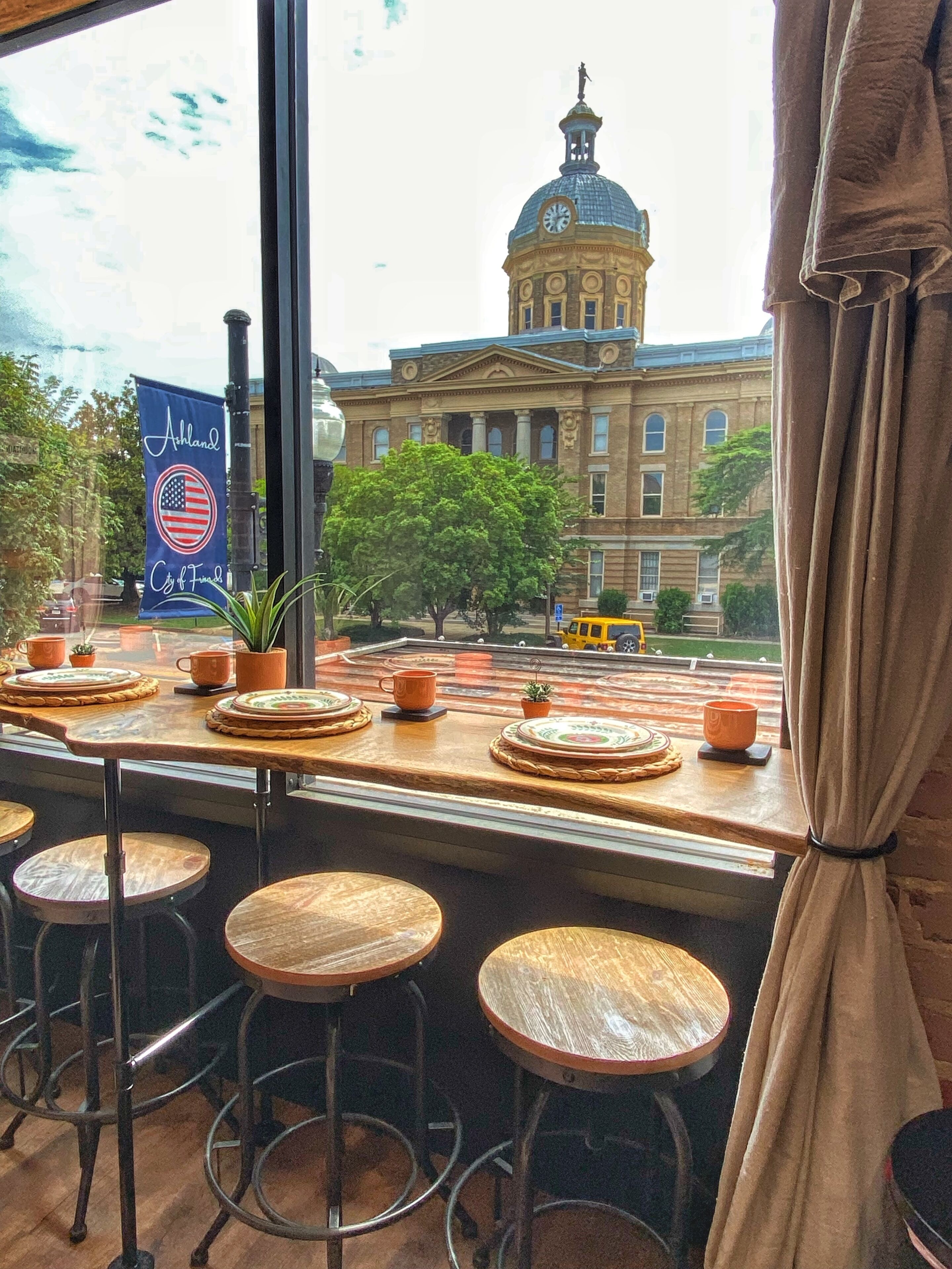 A restaurant with a view of a historic building, bar stools, and a flag.