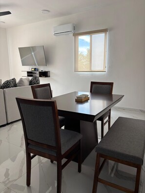 A modern dining area with a rectangular table, four chairs, and a television mounted on the wall.