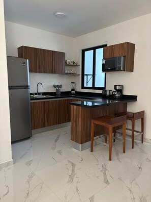 A modern kitchen with wooden cabinets, a built-in microwave, a refrigerator, a sink, and a marble-tiled floor.