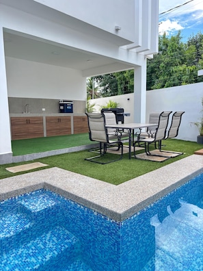 A modern outdoor kitchen with a grill, dining table, and chairs. - Privada Huayacán Cancun (Cancun)