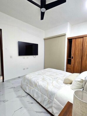 Un dormitorio con una cama, ventilador de techo, televisión montada y armario.