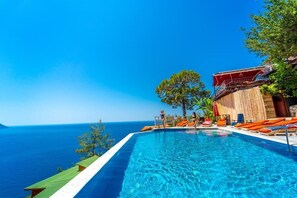 A pool with clear blue water, a wooden deck, and a view of the ocean.