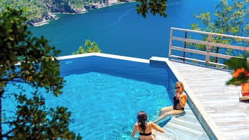 A pool with clear blue water, a wooden deck, and a view of the sea.