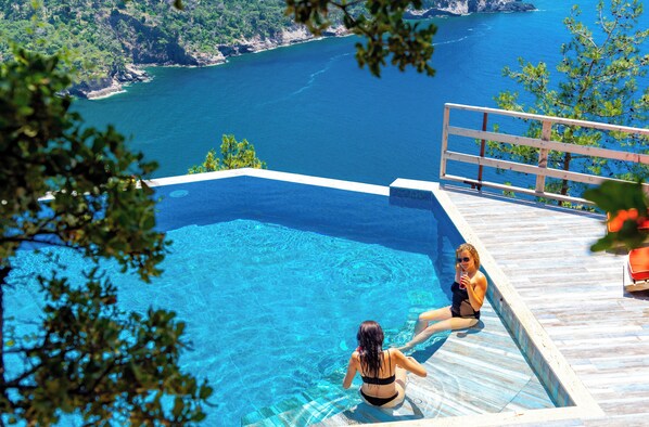 A pool with clear blue water, a wooden deck, and a view of the sea.