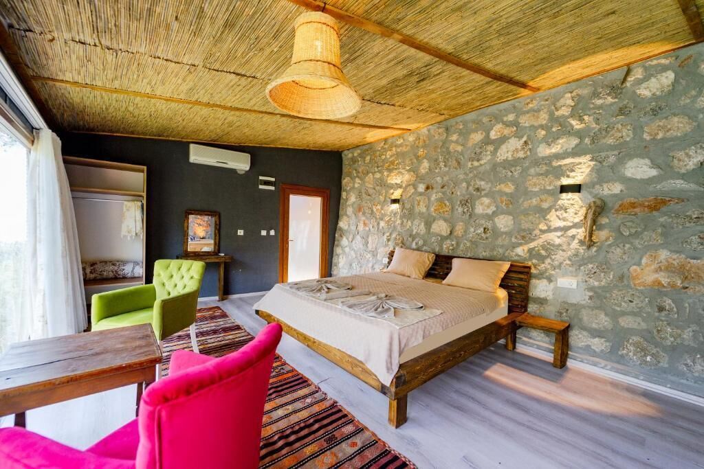 Ein Schlafzimmer mit einem Bett, einem Sessel, einem Tisch und einer Steinwand.