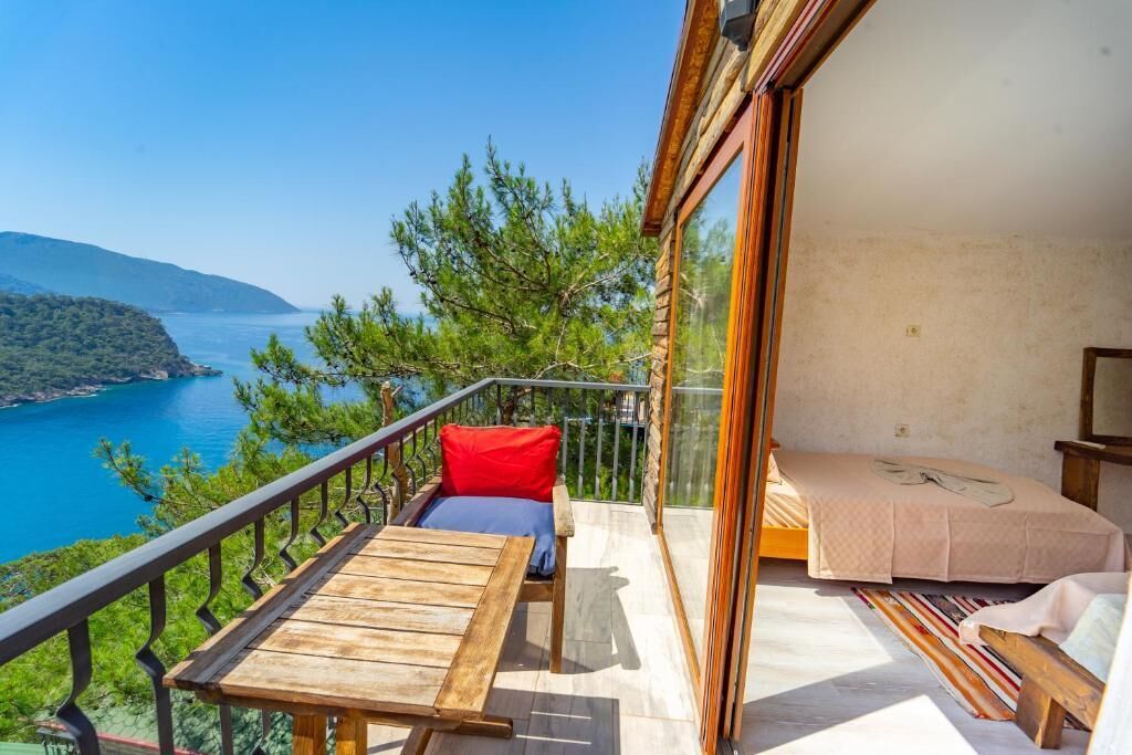 Un balcone con un tavolo e sedie di legno, un letto e vista su un lago e montagne.