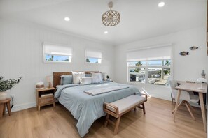 A bedroom with a bed, bedside tables, a bench, a desk, and a view of the outside. - Waterfront Hideaway · 100-Ft Dock · Hot Tub with TV — Your Keys Escape (Key Largo)