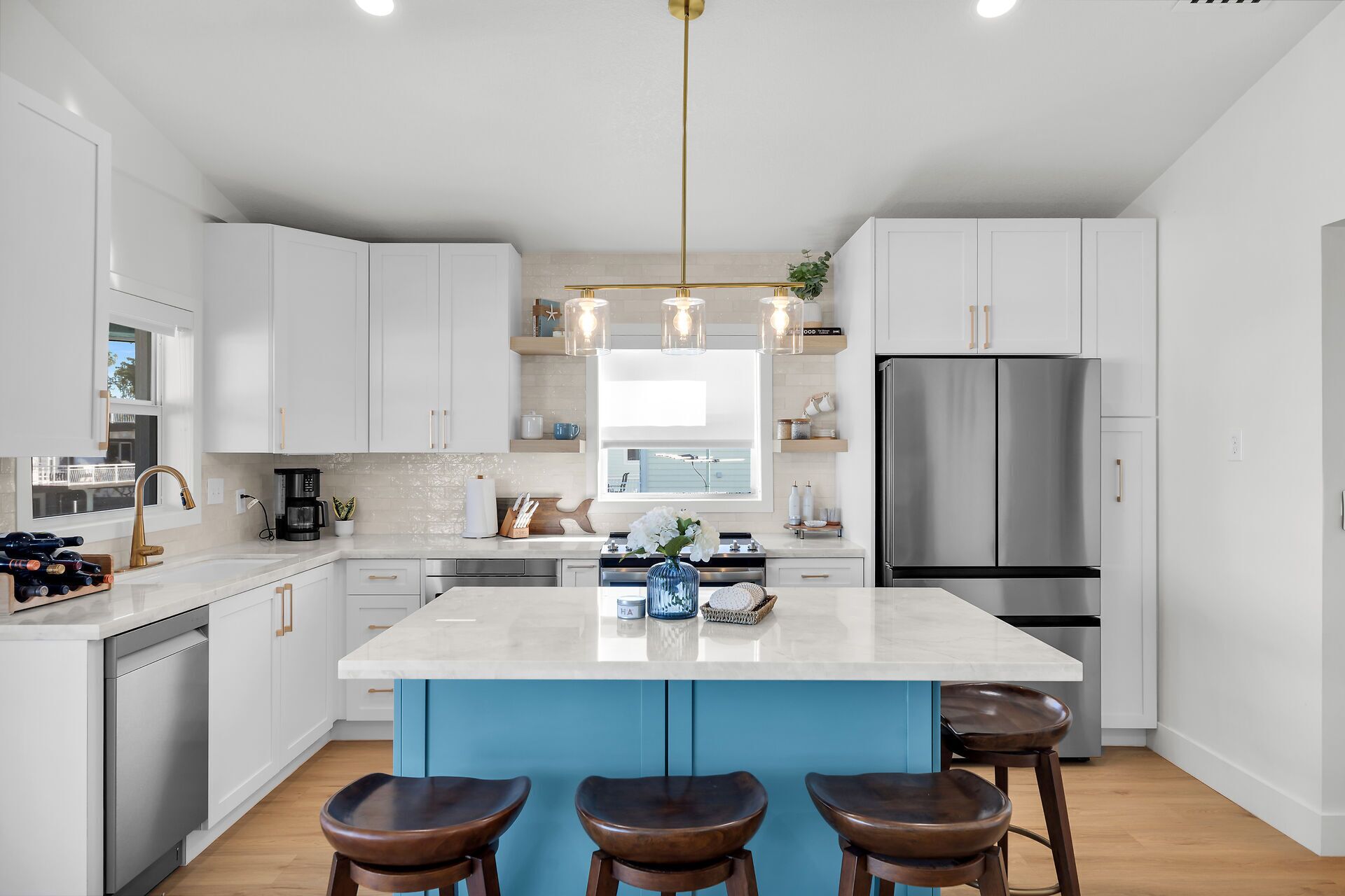 A modern kitchen with white cabinets, a stainless steel refrigerator, a central island with stools, and pendant lighting.