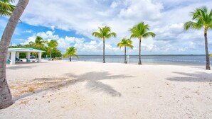 A beach with palm trees and a covered area with a car parked inside. - Waterfront Hideaway · 100-Ft Dock · Hot Tub with TV — Your Keys Escape (Key Largo)