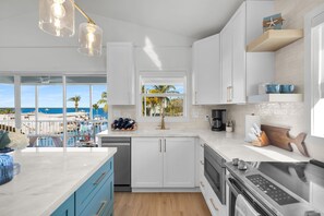 A modern kitchen with a view of the sea, white cabinets, and a large window. - Waterfront Hideaway · 100-Ft Dock · Hot Tub with TV — Your Keys Escape (Key Largo)