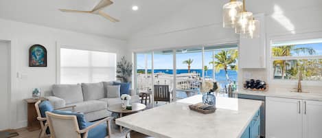 A modern kitchen with a large island, white cabinetry, and a view of the ocean.
