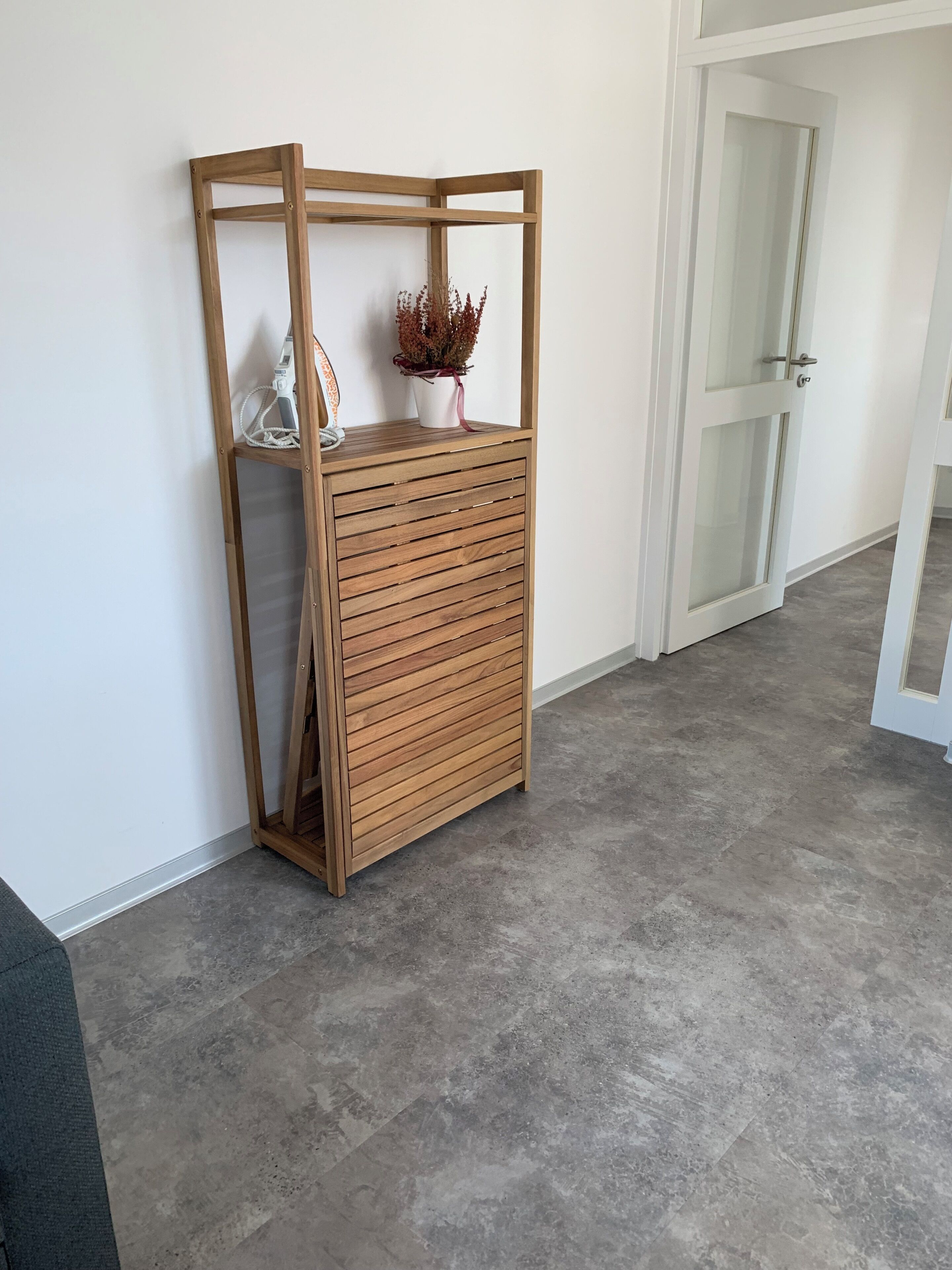 A corner room with a wooden storage unit against the wall, a potted plant, and a door leading to another room.