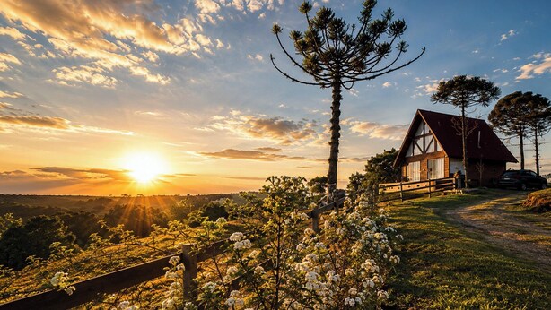 Una casa con techo inclinado, rodeada por una cerca de madera y una vista despejada del cielo.