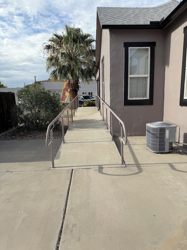 A concrete pathway leading to a building with a palm tree and a sign that reads 'SALE.'