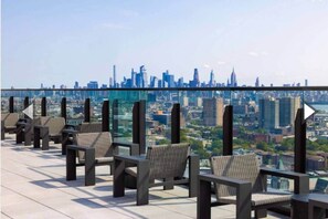 A rooftop terrace with wicker chairs and a city skyline view. - 10 Min Soho NYC Comfort Suite (Jersey City)