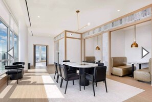 A modern hotel room with a large window, a round dining table, and a seating area with sofas. - 10 Min Soho NYC Comfort Suite (Jersey City)