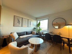 A modern living room with a sofa, a round coffee table, and a dining area with chairs and a table. - 10 Min Soho NYC Comfort Suite (Jersey City)