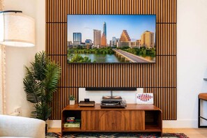 A modern living room with a flat-screen TV mounted on a wooden panel wall, a small wooden entertainment unit below, and a potted plant to the left. - Mid-Century Tiny House (Austin)