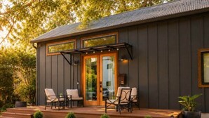 A modern house with a deck, outdoor seating, and a large glass door. - Mid-Century Tiny House (Austin)