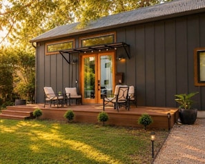 A modern house with a deck, outdoor seating, and a large glass door. - Mid-Century Tiny House (Austin)