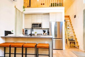 A modern kitchen with a central island, stainless steel appliances, and a wooden ladder leading to an upper level. - Mid-Century Tiny House (Austin)