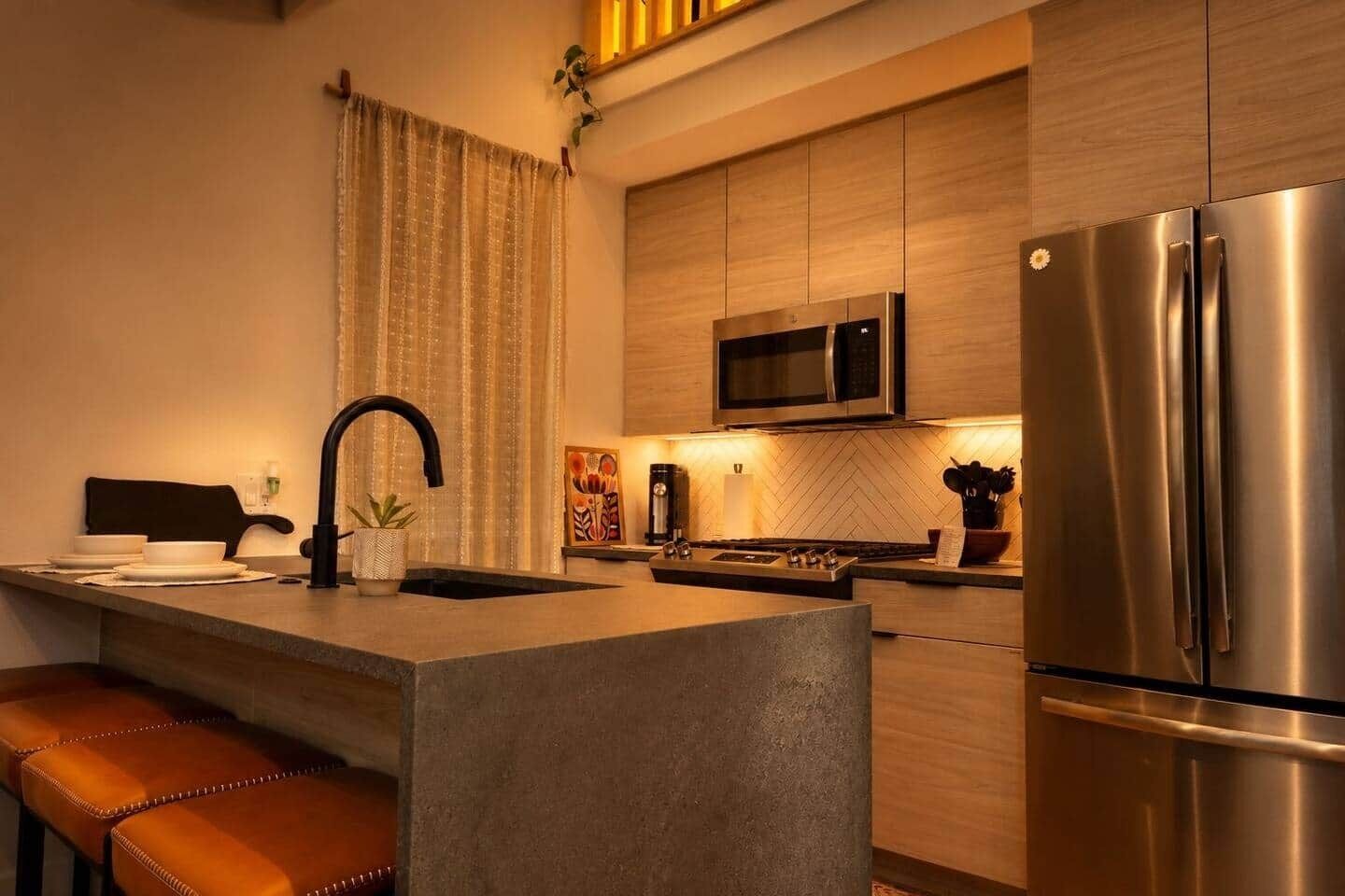 A modern kitchen with a central island, stainless steel appliances, and a herringbone wood backsplash.