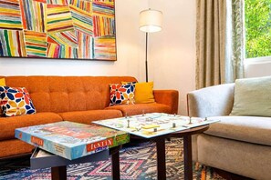 A living room with an orange sofa, a coffee table with a board game, a floor lamp, and a colorful abstract painting on the wall. - Mid-Century Tiny House (Austin)